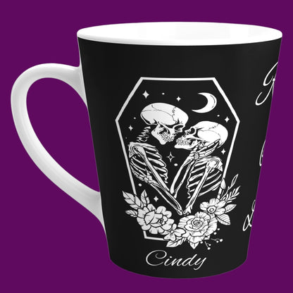 A custom matte black ceramic coffee mug with a white interior, featuring two skeletons in embrace with the phrase "Rest In Love" written in elegant white cursive script down the center. Personalize in The Fright Factory New Orleans.