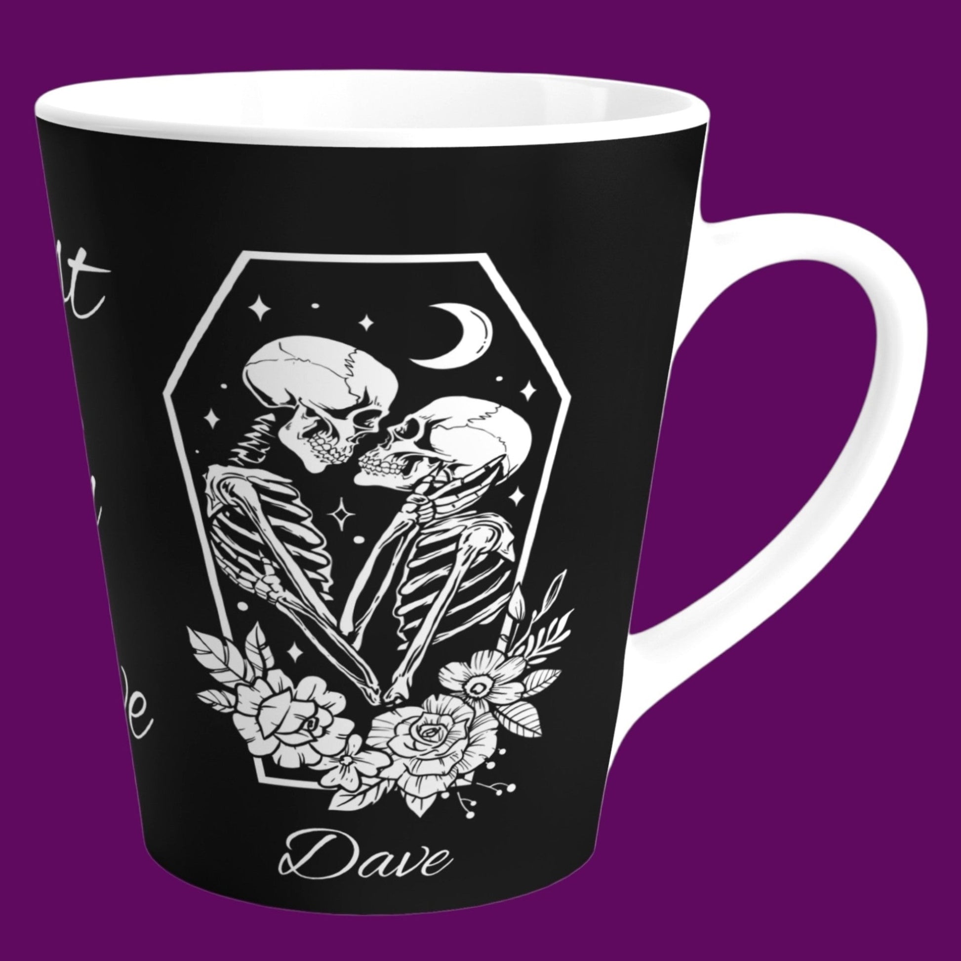 A gothic matte black ceramic coffee mug with a white interior, featuring two skeletons in embrace with the phrase "Rest In Love" written in elegant white cursive script down the center. Personalize in The Fright Factory New Orleans.